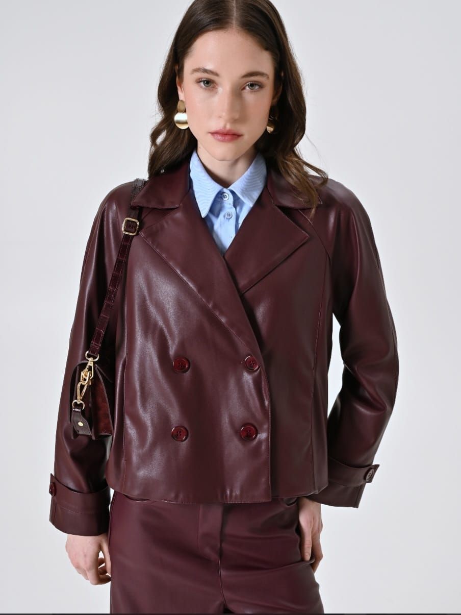Bordeauxrode dubbelrij leren jas over een lichtblauwe blouse.