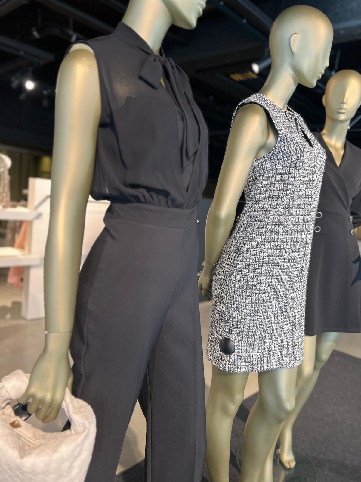 Paspoppen in een donkere blouse en een grijze tweedjurk in de showroom.