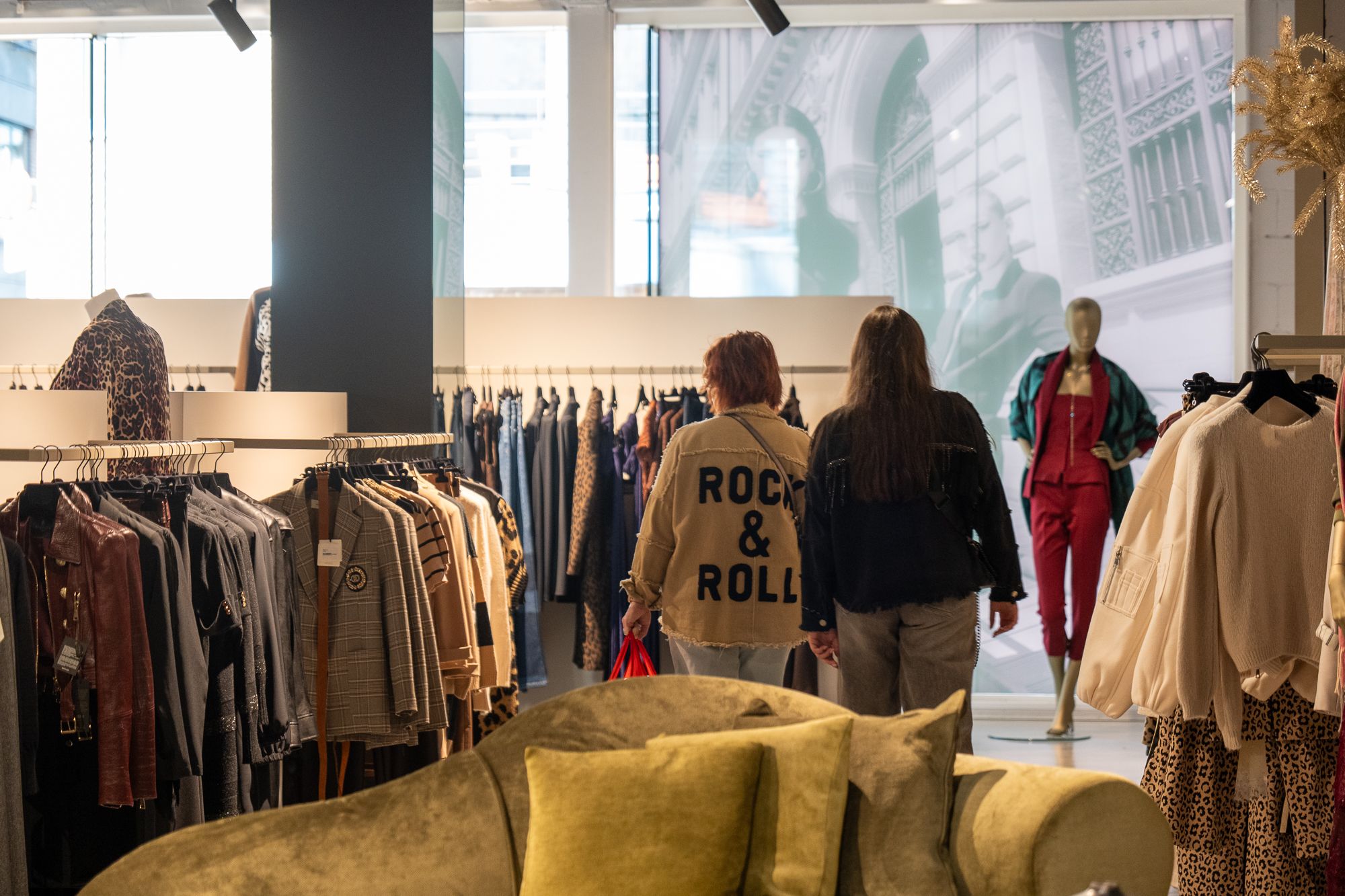 Klanten bekijken kledingrekken in de boetiek, met zicht op de straat door de open vitrine.