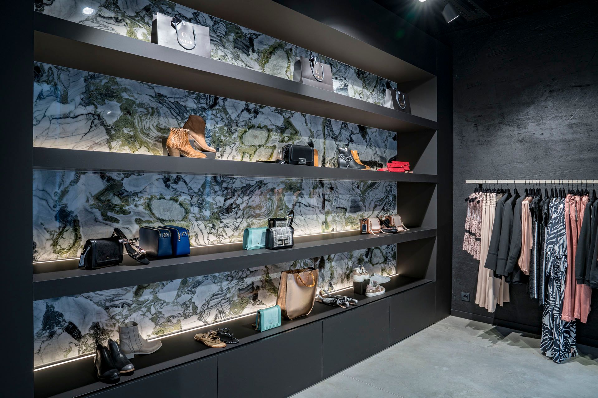 Verlichte wandplanken met handtassen en schoenen tegen een marmeren achterwand.