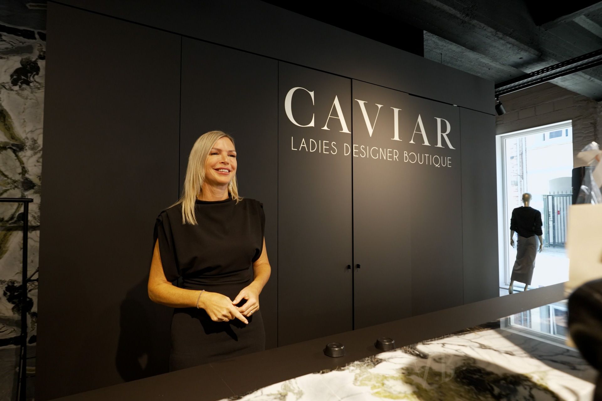 Medewerkster verwelkomt bezoekers aan de balie van CAVIAR, voor het opschrift ‘Caviar Ladies Designer Boutique’.
